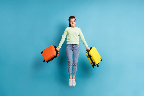 Full length body size photo of jumping girl keeping colorful suitcases before flight in airport isolated on vivid blue color background - Foto, afbeelding