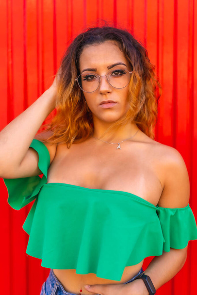 Lifestyle, Caucasian blonde girl in green T-shirts and transparent see glasses on a red background. With a seductive look at the summer photoshoot - Фото, зображення