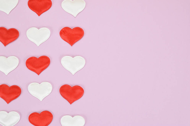 Red and white hearts on a pink background, arranged in three rows on the left side of the image - Фото, зображення