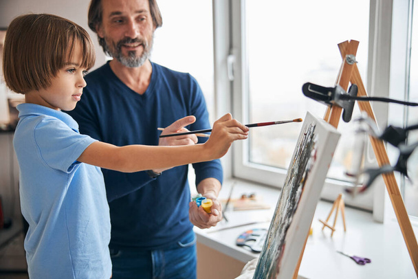 Concentrado criança pintura na tela ao lado de seu pai - Foto, Imagem