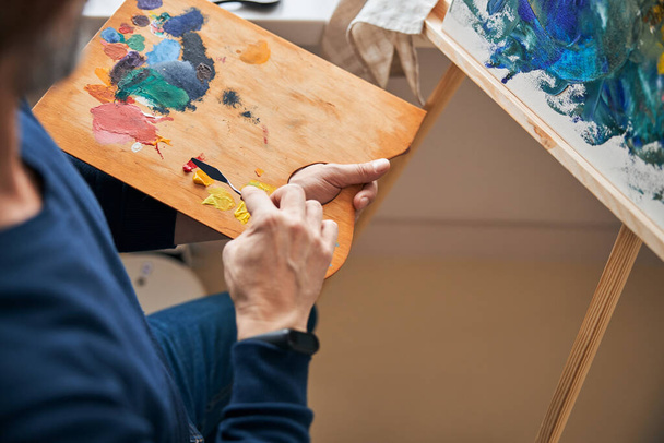 Выделенный художник смешивает цвета для живописи на холсте - Фото, изображение