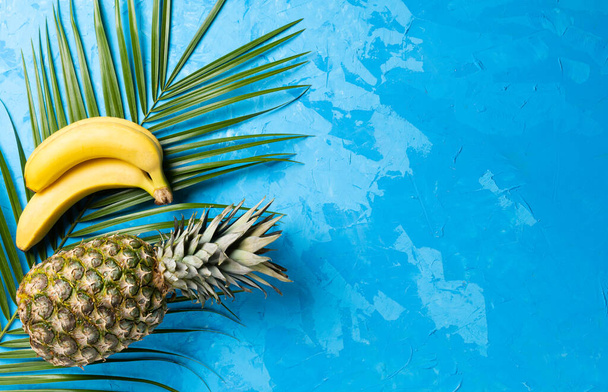 Pineapple,banana and tropical palm leave on blue cement background. Top view - Foto, Imagen