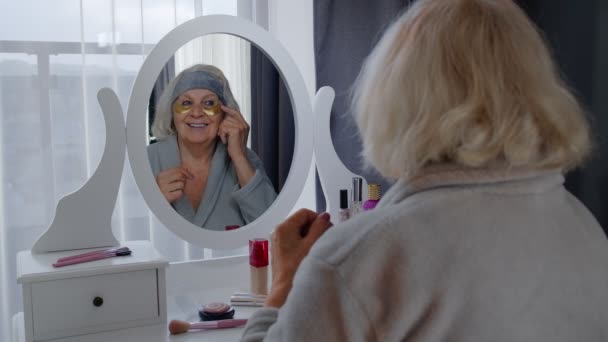 Oud bejaarde vrouw grootmoeder toepassen anti-rimpel ooglapje, het zetten van make-up op thuis - Video