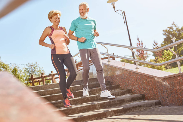 Healthier and Happier. Full length shot of active mature family couple in sportswear looking happy while jogging together on a warm sunny day. Joyful senior couple doing sport outdoors - Photo, Image