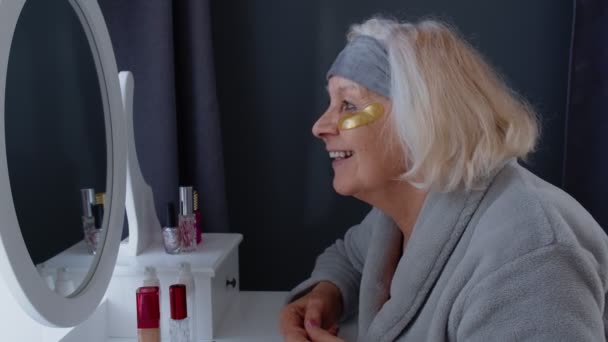 Yaşlı, yaşlı bir kadın, kırışıklık önleyici göz bandı takıyor, evde makyaj yapıyor. - Video, Çekim