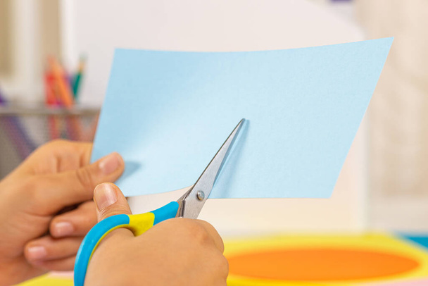Kid hands cutting colored paper with scissors. Education, learning, paper craft, entertainment at home - Photo, Image
