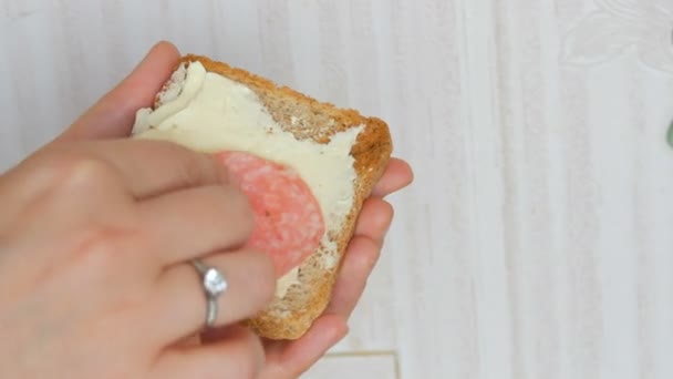 Une main de femme met de minces morceaux de saucisse de salami sur une tranche de pain grillé. Petit déjeuner matinal - Séquence, vidéo