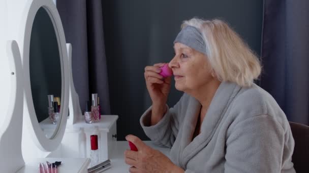 Anciana abuela anciana cuidando de la piel, aplicando base antiarrugas con esponja - Metraje, vídeo