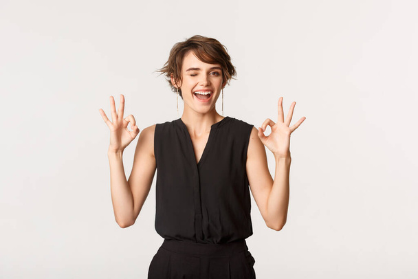 Sassy good-looking young woman assure you, showing okay gesture and winking, standing white background - Photo, Image