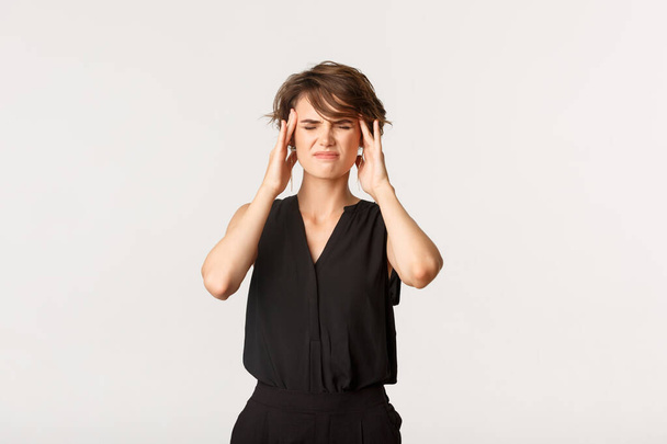 Junge Geschäftsfrau berührt Schläfen und Grimassen von schmerzhafter Migräne. Mädchen klagt über Kopfschmerzen, weißer Hintergrund - Foto, Bild