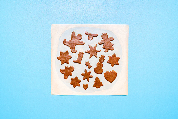 Baking cookies flat lay with gingerbread dough cut in many shapes, on a baking paper, on blue background. Raw gingerbread man and star shape cookies. - Photo, Image