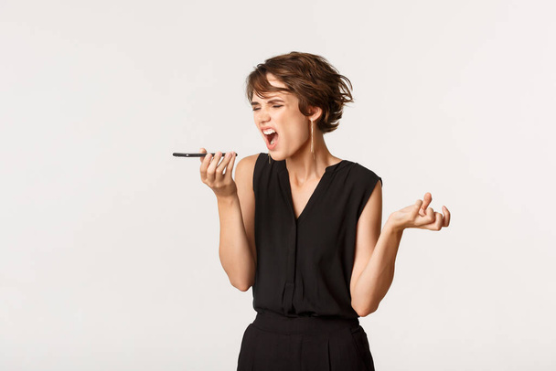 Angry woman shouting, recording voice message, yelling at someone over phone call, standing white background - Photo, Image