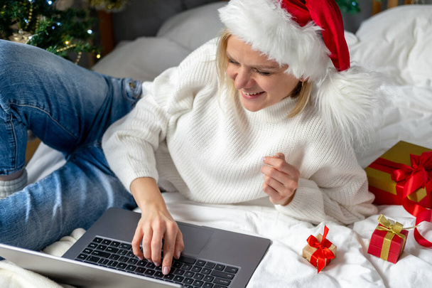 Christmas online shopping. Female buyer makes order on laptop. Woman buy presents, prepare to xmas, among gift boxes and packages. Winter holidays sales. - Fotó, kép