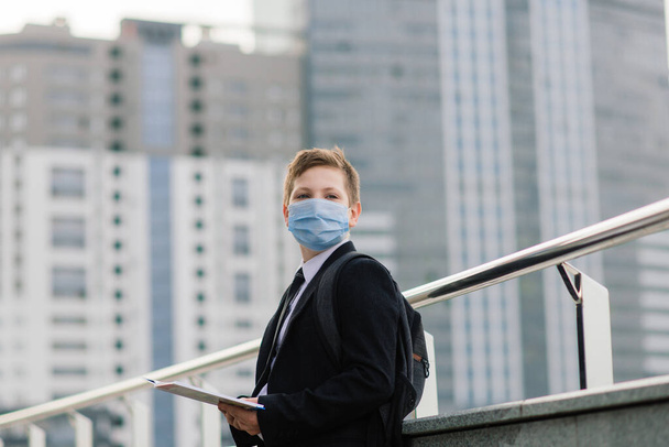 Schoolboy walks out of school wearing protective mask in the city - Foto, Imagen