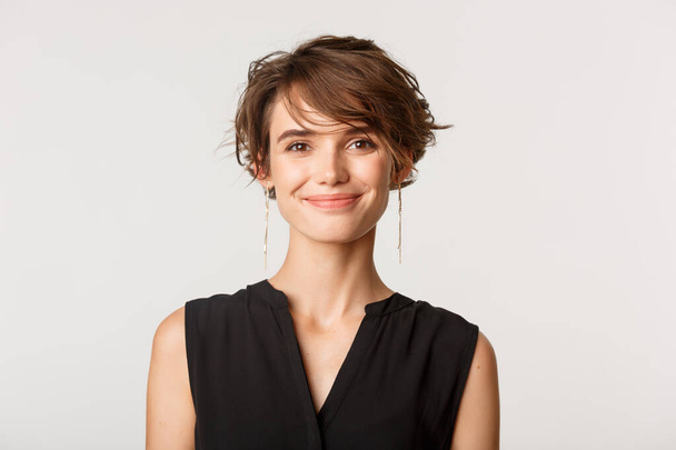 Close-up of attractive fashionable woman smiling at camera, standing over white background - Фото, зображення