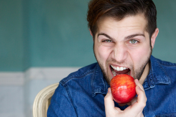 Handsome young man eating red apple  - Foto, Bild