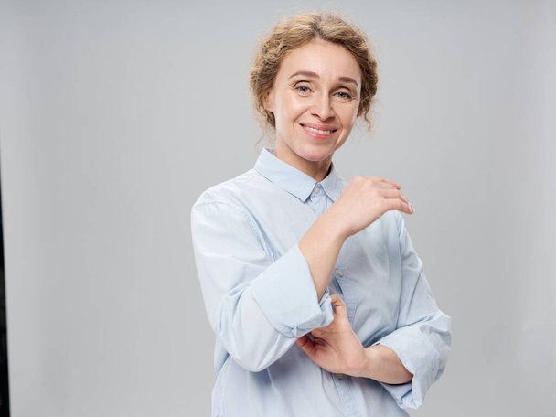 Elderly woman in a light shirt on a gray background smiling at the camera - Foto, imagen