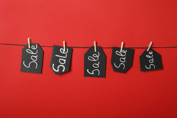 Tags with word Sale hanging on rope against red background. Black Friday concept - Foto, Bild