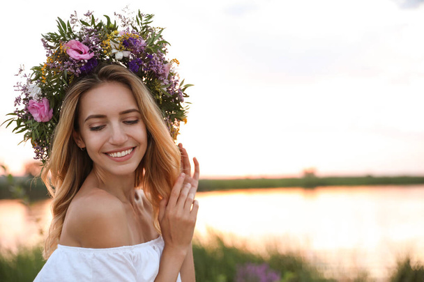 Young woman wearing wreath made of beautiful flowers outdoors at sunset - Foto, Imagem