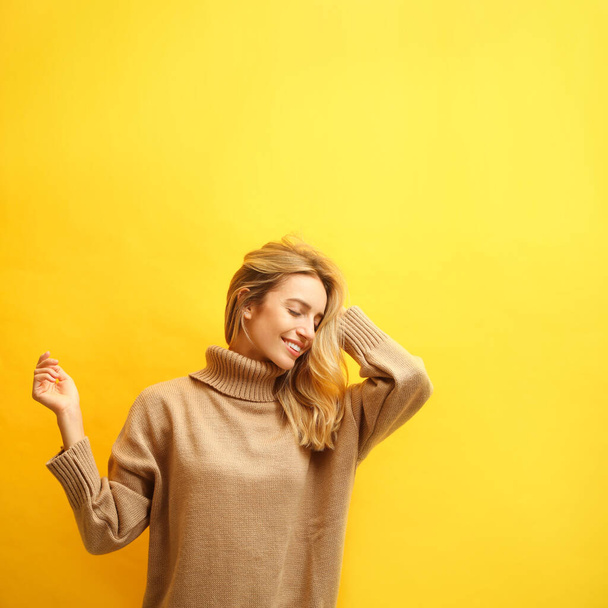 Beautiful young woman wearing knitted sweater on yellow background - Fotó, kép