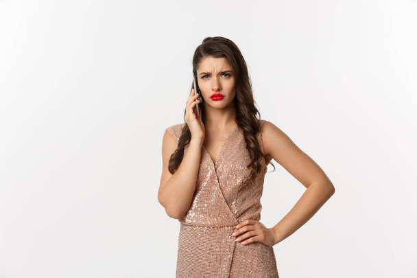 Christmas party and celebration concept. Elegant woman in glamour dress talking on phone and looking displeased, receive bad news, white background - Foto, immagini