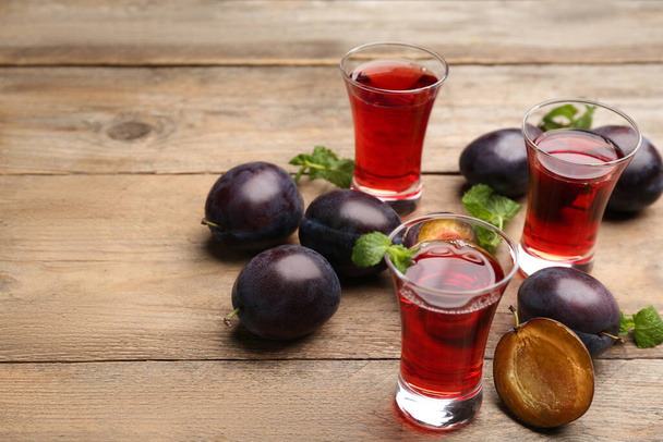 Delicious plum liquor, mint and ripe fruits on wooden table. Homemade strong alcoholic beverage - Foto, Imagen