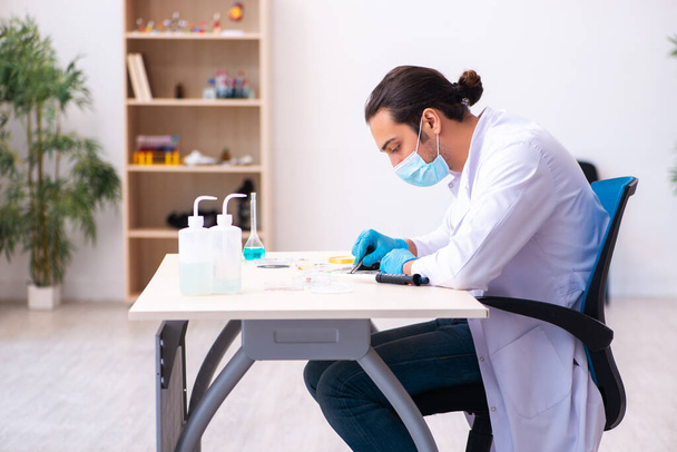 Joven químico masculino trabajando en el laboratorio durante una pandemia - Foto, imagen