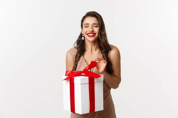 Frohe Weihnachten. Charmante Frau im eleganten Kleid offene Geschenkbox und lächelt erfreut, Auspacken eines Geschenks, steht über weißem Hintergrund - Foto, Bild