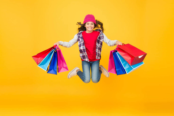 Happy little girl jump with shopping bags yellow background, sale - Fotografie, Obrázek