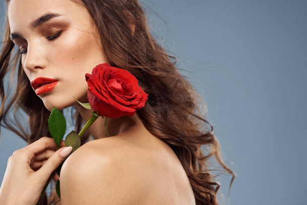 Portrait of a woman with a red rose in her hands on a gray background naked shoulders evening makeup - Фото, зображення