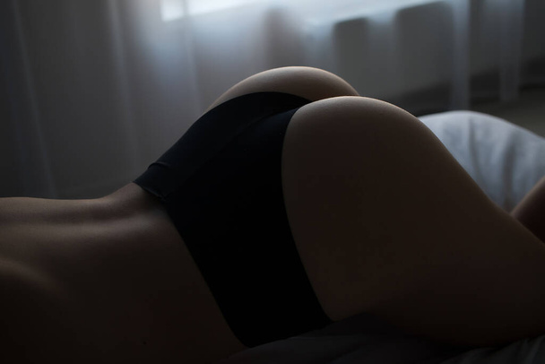 Back view of slim sexual nude woman in panties lying on bed in room - Photo, Image