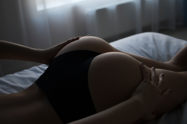 Вид сзади на стройную сексуальную обнаженную женщину в трусиках лежащую на кровати в комнате - Фото, изображение