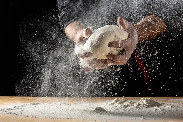 Руки пекаря замішують тісто ізольовано на чорному тлі. готує екологічно чисту випічку
. - Фото, зображення