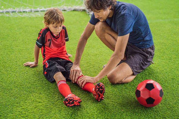 Little cute kid boy in red football uniform and his trainer or father playing soccer, football on field, outdoors. Active child making sports with kids or father, Smiling happy boy having fun in - Zdjęcie, obraz