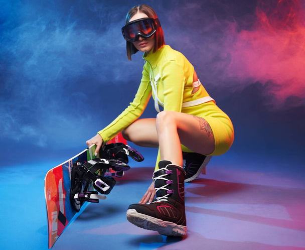 Cute girl with ski glasses and snowboard poses in studio - Photo, Image
