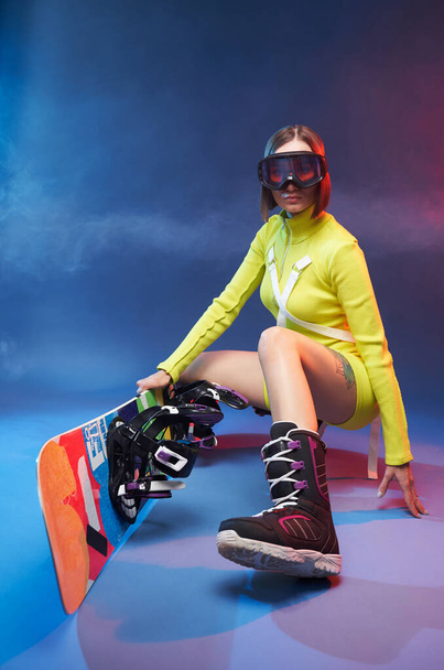 Sportief schattig meisje met snowboard poses in smokey achtergrond - Foto, afbeelding