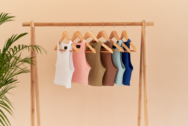 color basic undershirt clothes hanging on wooden hangers. fabric and textile close up on shirts with no sleeves. top crop shirt; - Photo, Image