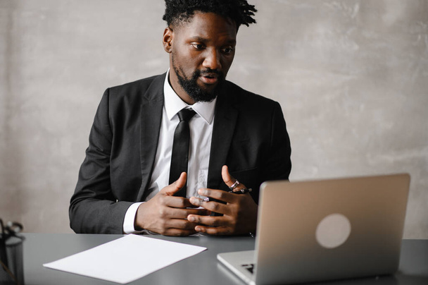 Focused black businessman in suit, holding video call with clients on laptop. Concentrated millennial man in suit giving online conference consulting customer - Foto, Imagem