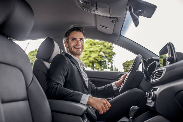 Smiling bearded male sitting at drivers seat, holding steering wheel - Fotó, kép