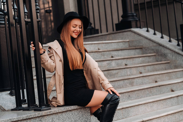 Stylish young woman in a beige coat in a black hat on a city street. Women's street fashion. Autumn clothing.Urban style. - Foto, afbeelding