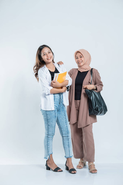 Portrait of a young woman smiling meeting a study friend carrying a bag and book - Foto, Bild