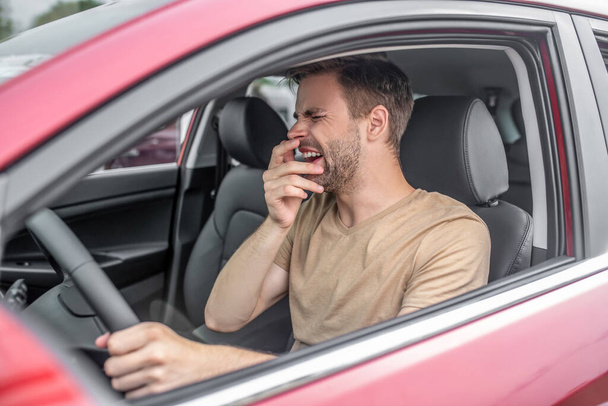Tired young male driving red car, yawning - Foto, Bild