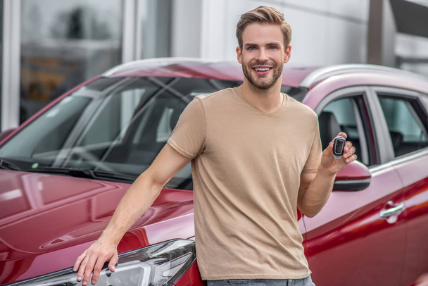 Smiling young male leaning on red car, holding keys - Foto, immagini
