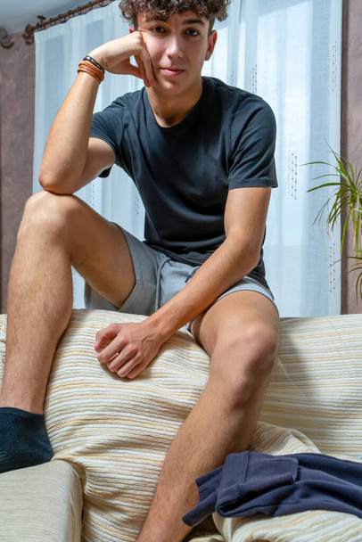 Attractive young man with curly hair wearing black t-shirt posing on white curtains background. Fashion concept - 写真・画像