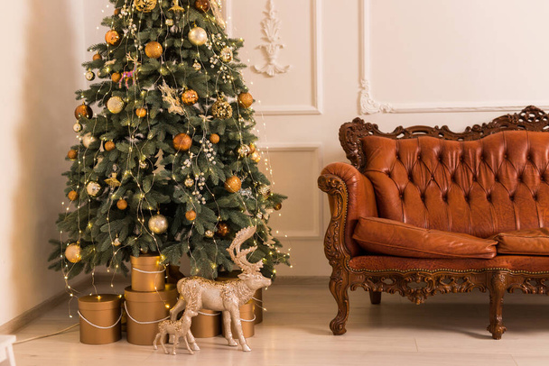 Close-up von Weihnachten Licht Innenraum Studio. Innenraum mit festlichem Baum mit Geschenken, Hirsch und braunem Sofa - Foto, Bild