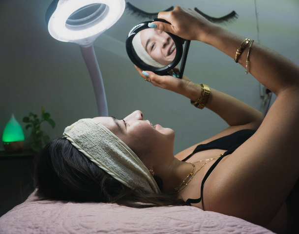 Νεαρή γυναίκα κοιτιέται στον καθρέφτη μετά τη θεραπεία προσώπου - Φωτογραφία, εικόνα