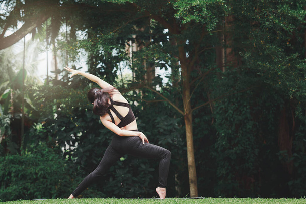Mujer asiática practicando yoga en Warrior Pose (Virabhadrasana) en la esterilla en el parque al aire libre. - Foto, Imagen