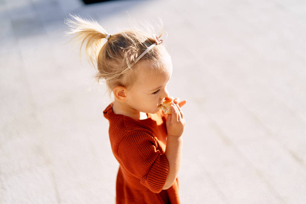 Een mooi klein meisje met een roze strik in haar haar eet een taart op een zonnige dag - Foto, afbeelding