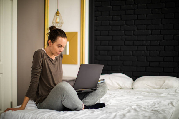 Adult woman using laptop on bed - Фото, изображение