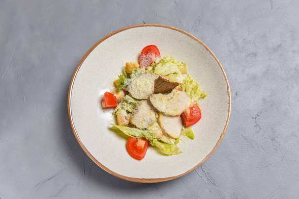 Bowl of Caesar Salad served on a black background in restaurant or diner. Traditional Caesar recipe. Eating out concept. - Foto, Imagen